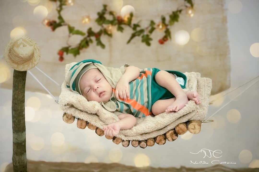 Ensaio fotógrafo infantil em estúdio produção rústica linda o bebê esta deitado em uma cama de madeira e no cenário tem um chapéu de palha e flores e flores  ao fundo fotógrafo  Naldo Caitano -Santas /SP