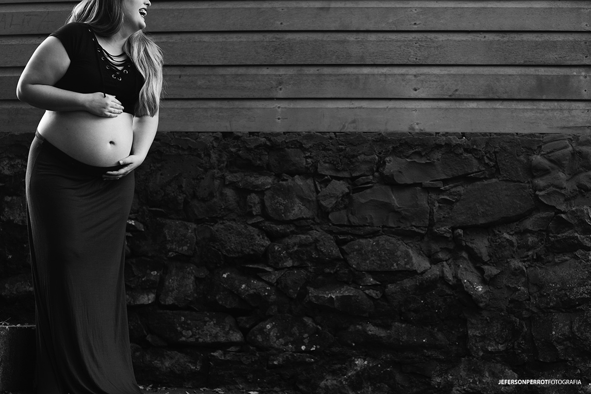 gravida sorridente com barriga a amostra em parede de madeira e pedras