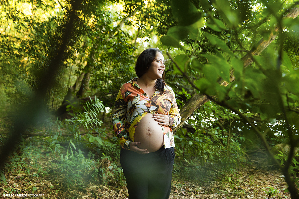 gestante no meio da vegetação em parque acariciando a barriga