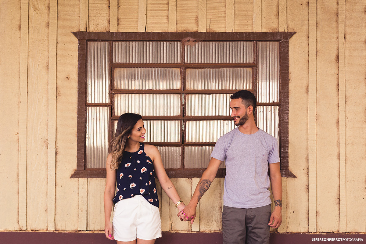 casal de mãos dadas em frente de janela em ensaio pré-casamento em mandaguacu, no parana