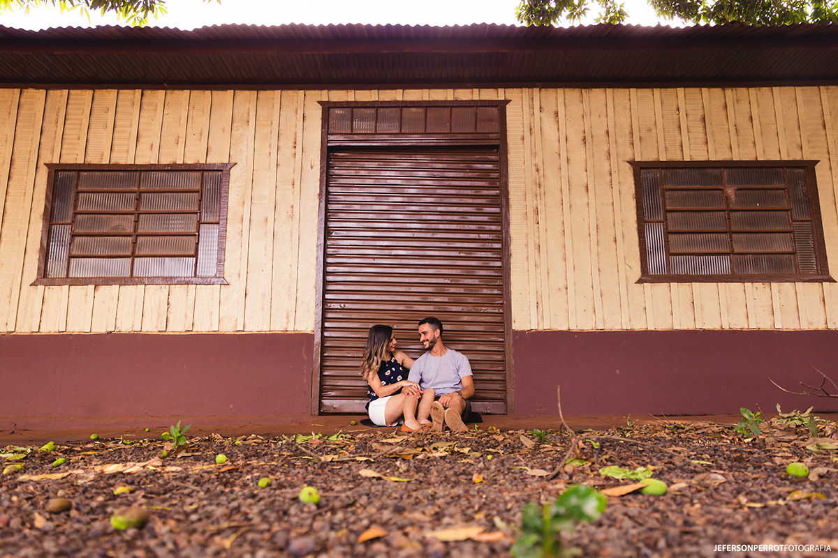 casal sentado em frente a uma velha mercearia durante ensaio pré-casamento em mandaguacu, no parana
