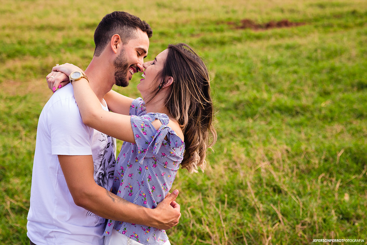 casal sorrindo abraçado em uma planície de gram