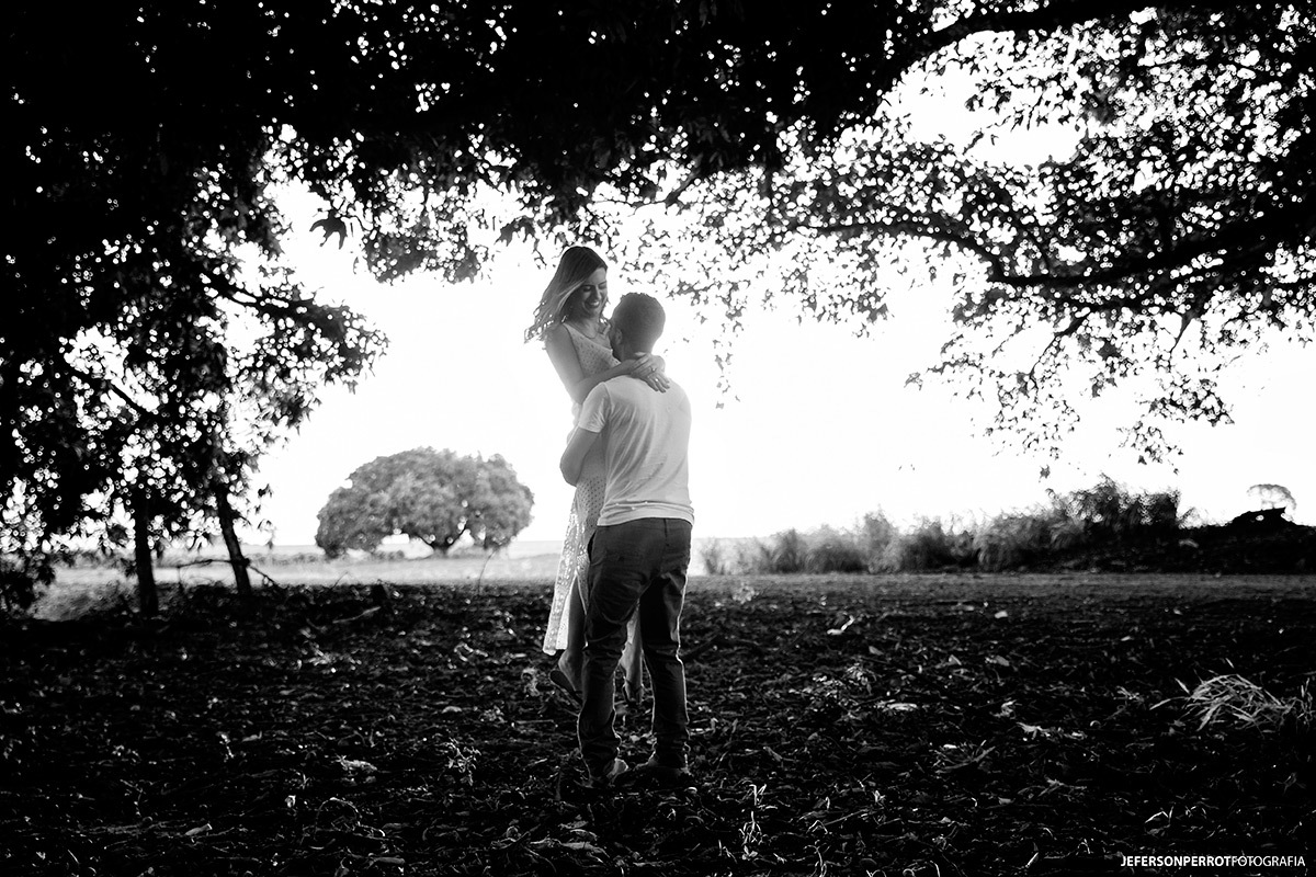 casal abraçado sobre folhas e em meio a grandes árvores em ensaio fotográfico 