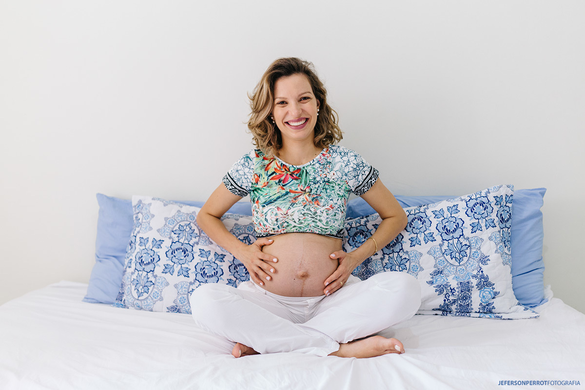 gestante sentada na cama sorridente com barriga a mostra