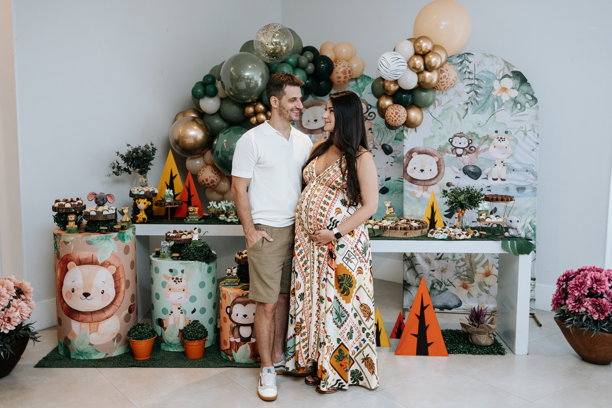 Foto panorâmica do casal em frente à mesa de doces completa.