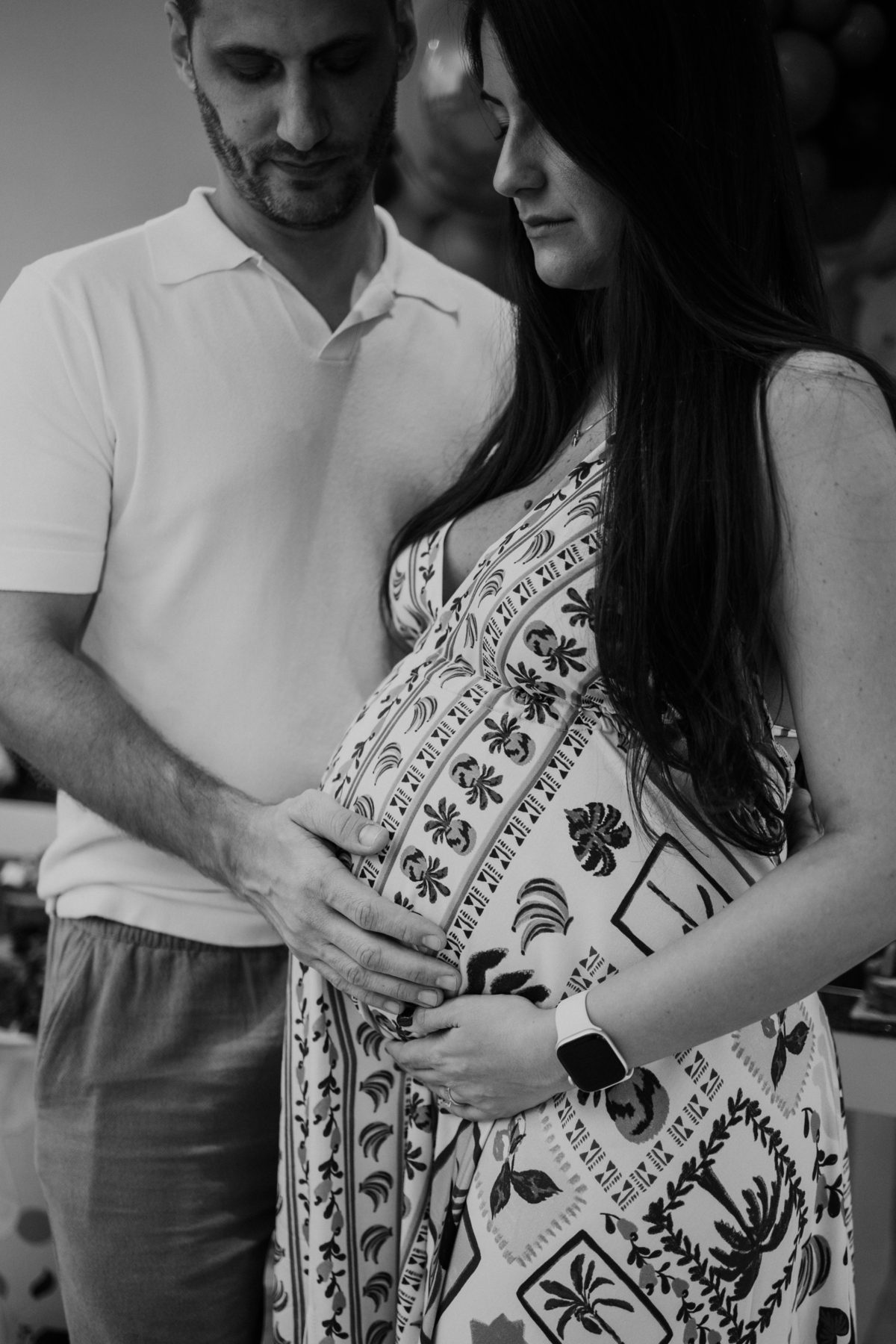 Foto em preto e branco com foco na barriga da gestante e mãos do casal.
