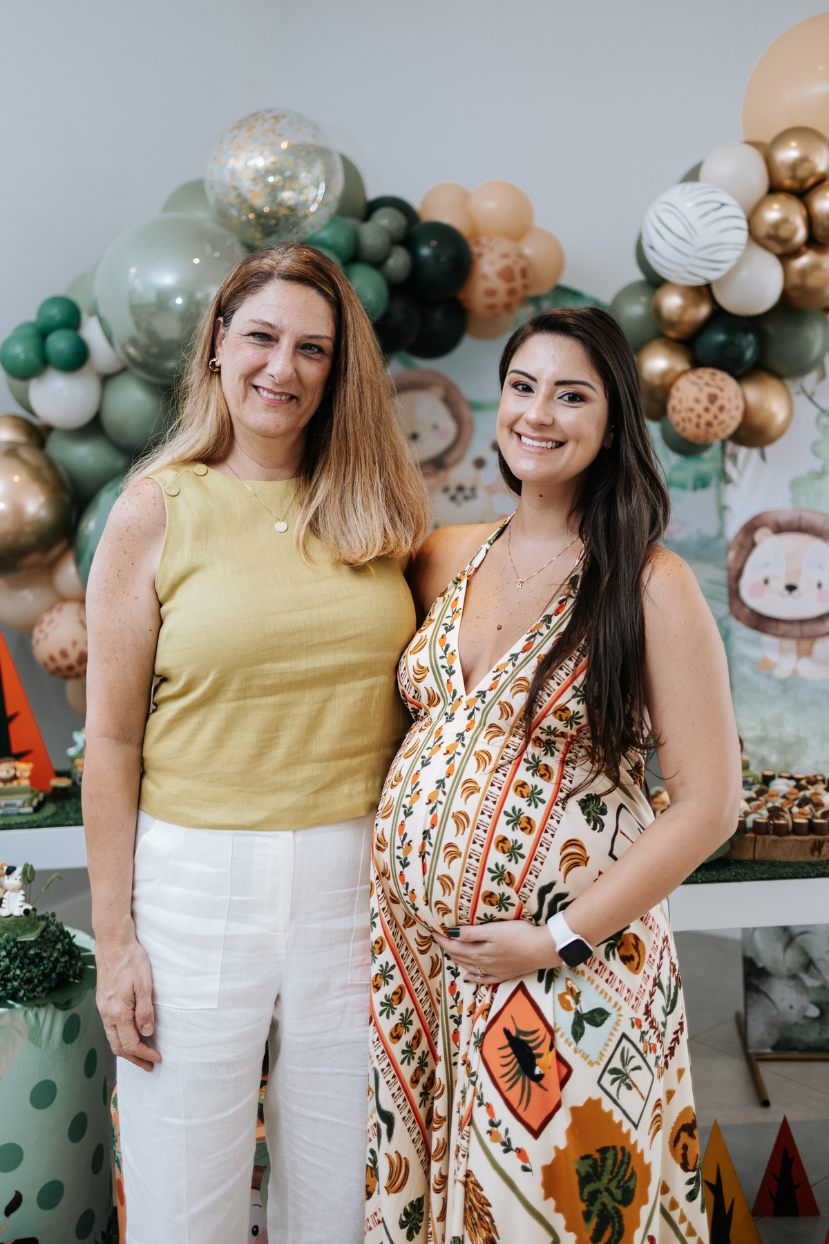 Foto da gestante posando com uma convidada em frente ao painel.