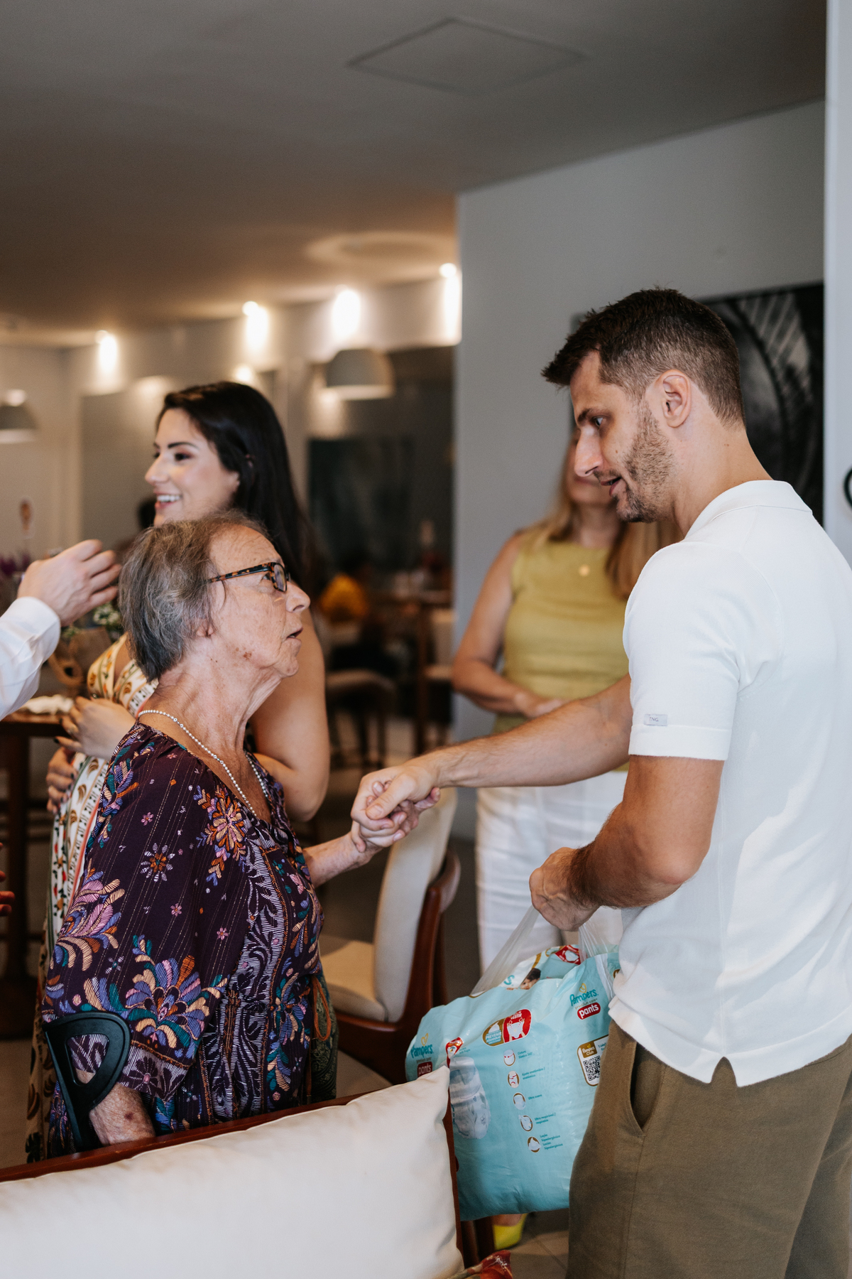 Foto do futuro papai interagindo e cumprimentando convidados idosos.
