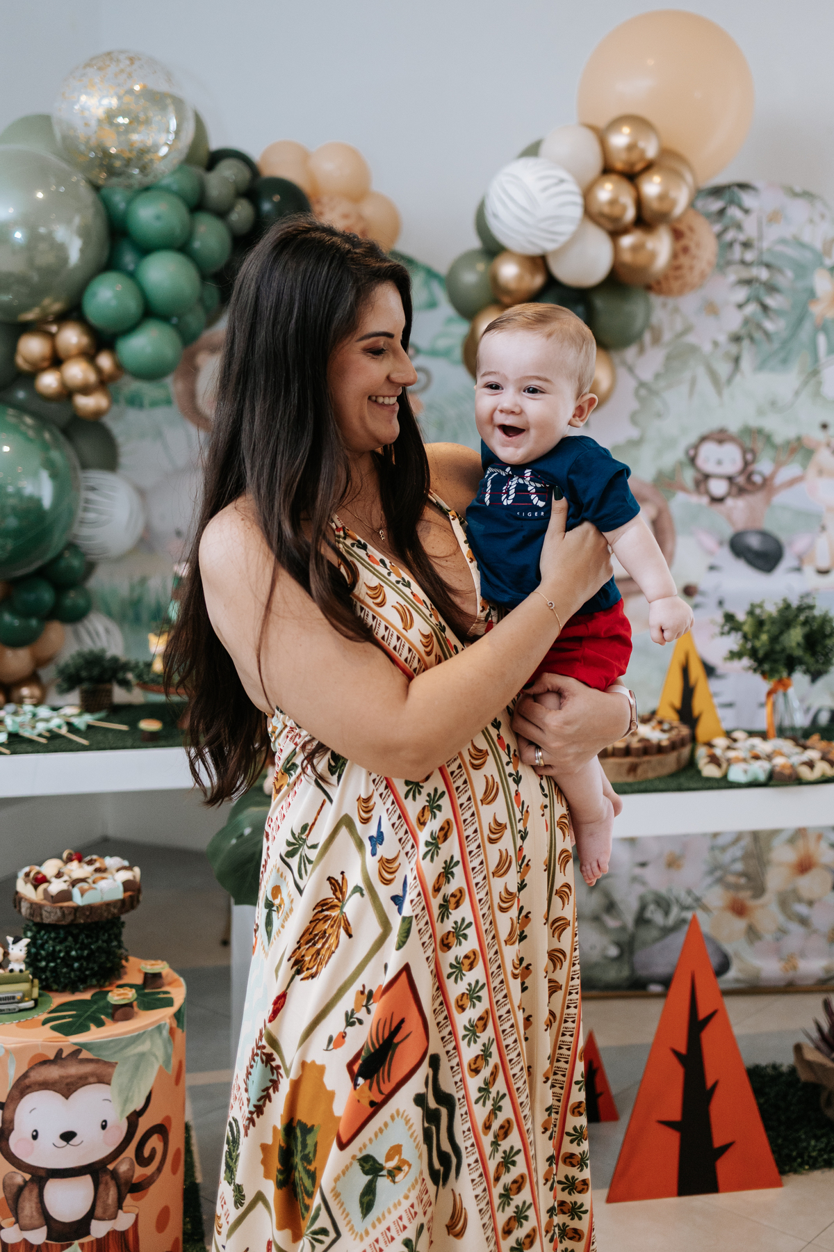 Foto da gestante sorridente segurando uma criança no colo na decoração Safari.