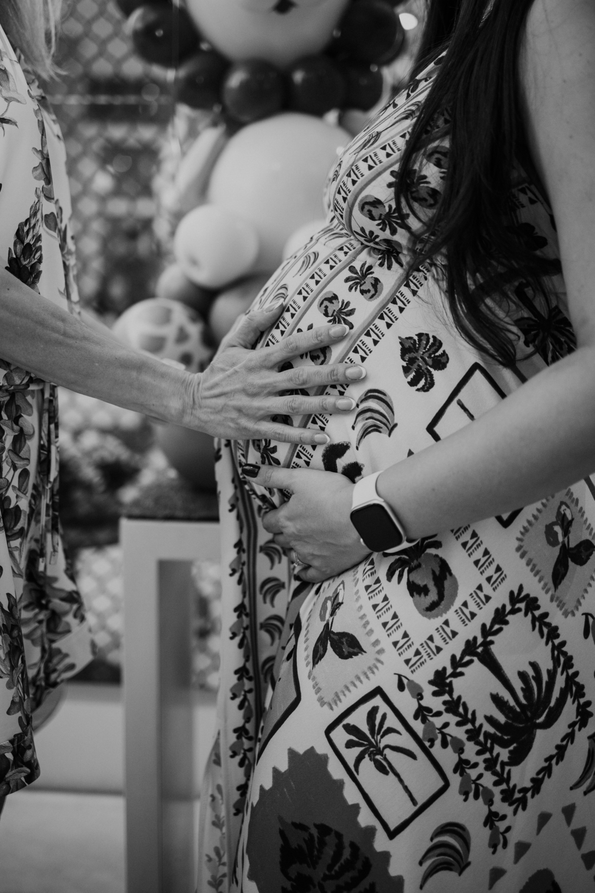 Foto em preto e branco com detalhe de mãos de familiares sobre a barriga.