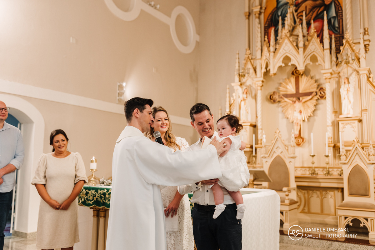A vela acesa simbolizando a luz de Cristo, sendo entregue aos pais durante a cerimônia de batizado, um momento de fé e esperança. Pais segurando a vela batismal acesa, em um momento de união e compromisso com a fé cristã.
