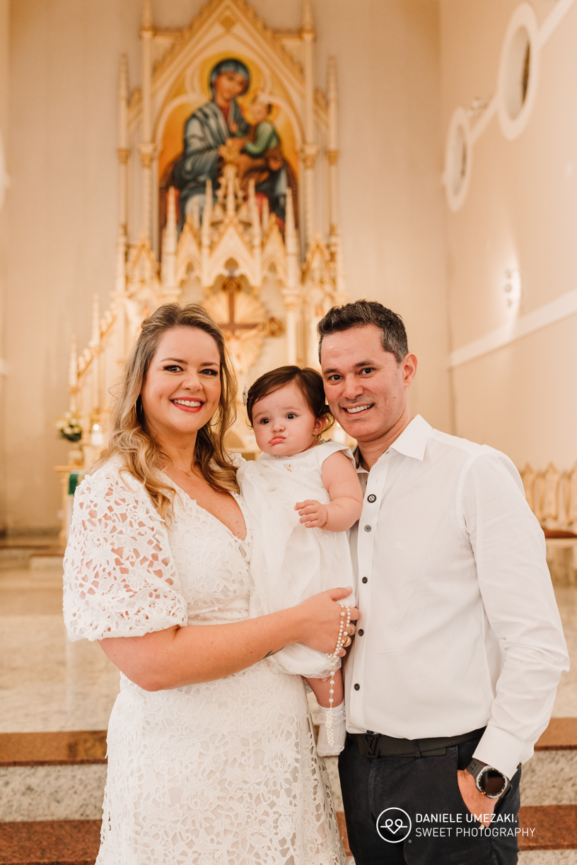 Família reunida diante do altar após o batizado, em um momento de gratidão e alegria.