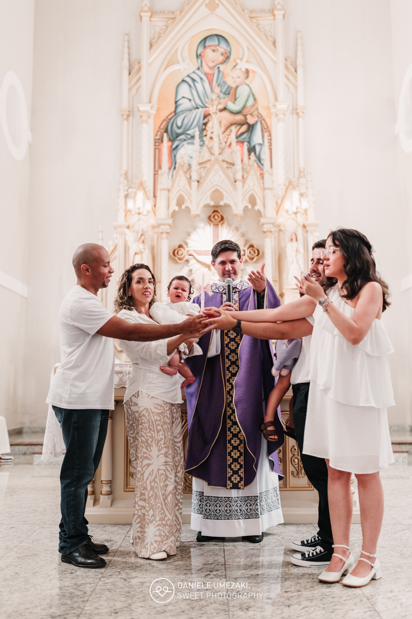 Pais com a bebê Alana no colo durante o batizado na Igreja do Socorro – registro de batizado com fotógrafa especializada em família