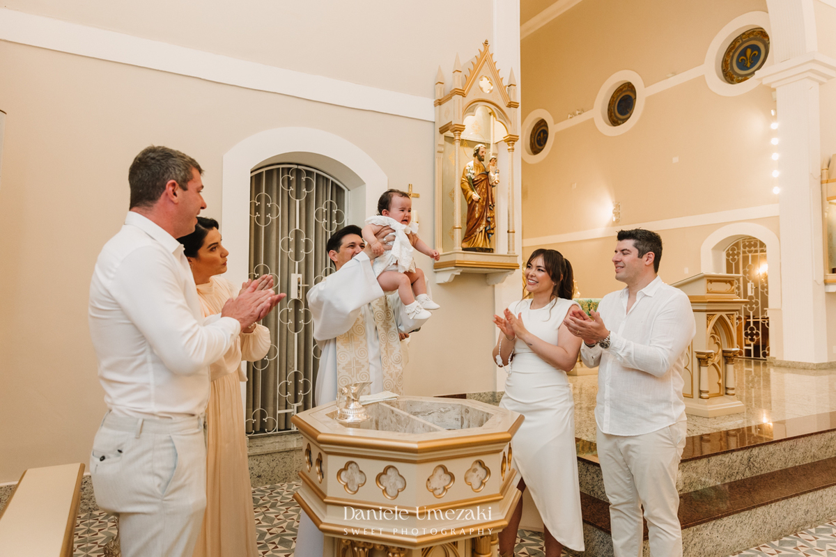 Fotografia de batizado na Igreja do Socorro, em Mogi das Cruzes. Cerimônia conduzida pelo Padre Michel, com almoço em família e decoração da Cerejeira Decora. Registro afetivo por Dani Umezaki