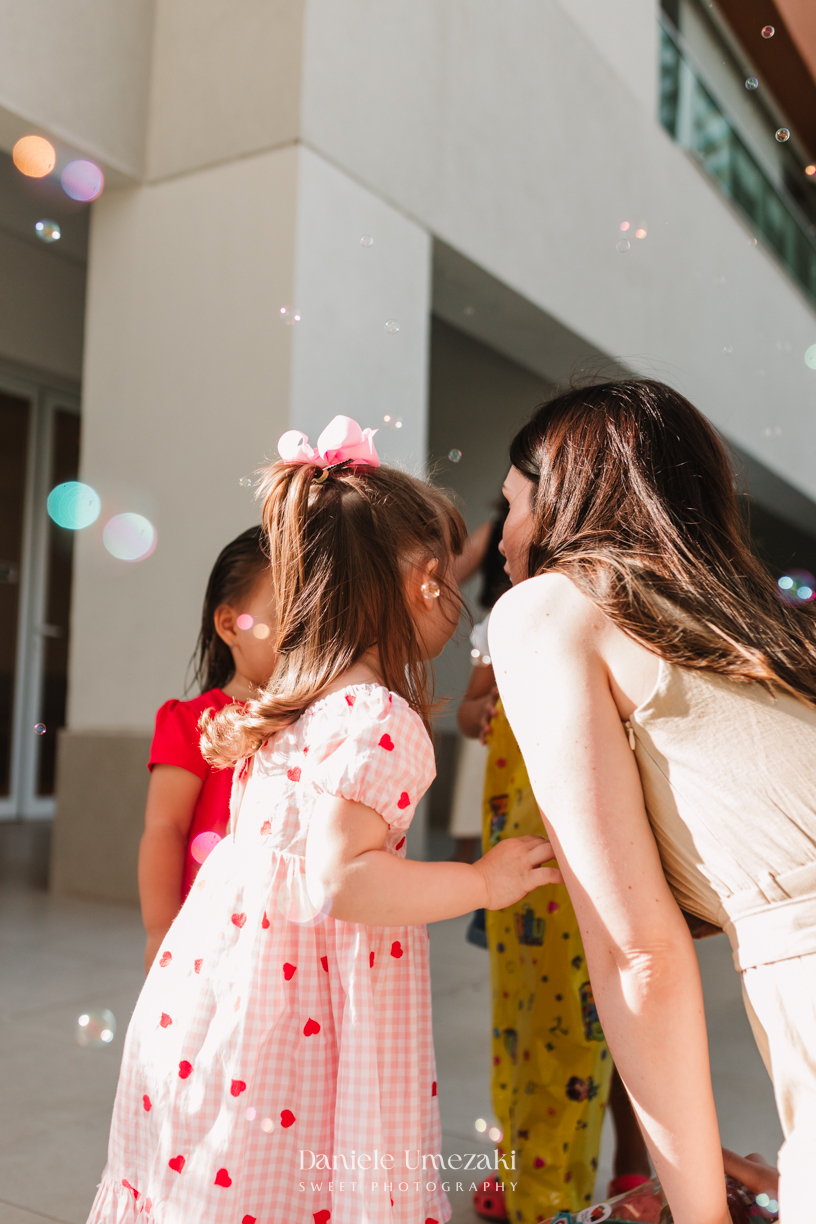 Aurora se divertindo com bolinhas de sabão durante seu aniversário de 2 anos. Fotografia de aniversário infantil em Mogi das Cruzes, com registros espontâneos e afetivos por Dani UmezakiAurora se divertindo com bolinhas de sabão durante seu aniversário de