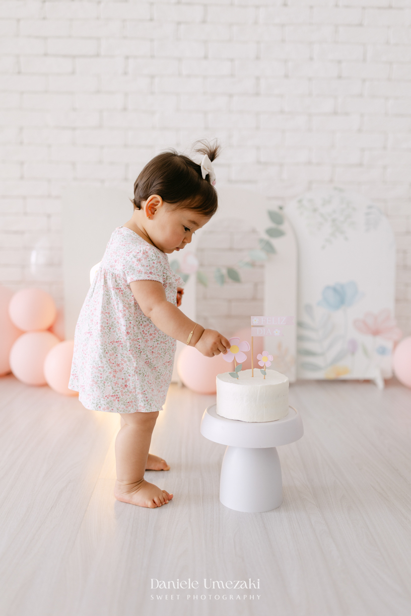Smash the Cake da Luiza realizado em estúdio em Mogi das Cruzes, com bolo da Ume Doces. Ensaio fotográfico infantil registrando os primeiros momentos do aniversário de 1 ano com leveza, diversão e afeto.