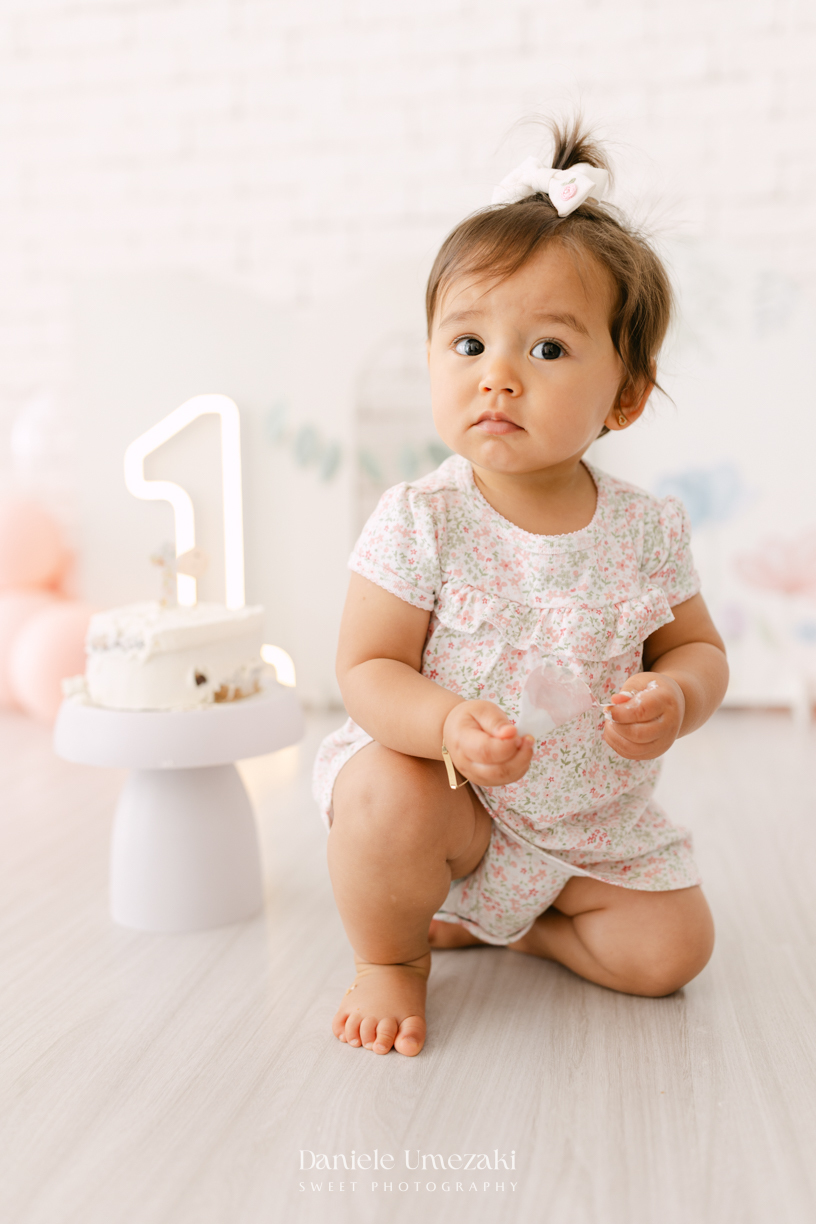 Smash the Cake da Luiza realizado em estúdio em Mogi das Cruzes, com bolo da Ume Doces. Ensaio fotográfico infantil registrando os primeiros momentos do aniversário de 1 ano com leveza, diversão e afeto.