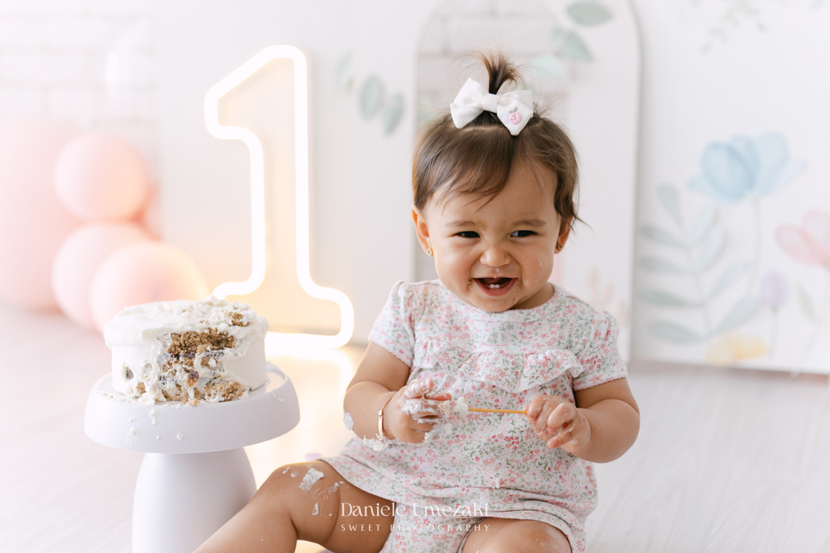 Smash the Cake da Luiza realizado em estúdio em Mogi das Cruzes, com bolo da Ume Doces. Ensaio fotográfico infantil registrando os primeiros momentos do aniversário de 1 ano com leveza, diversão e afeto.