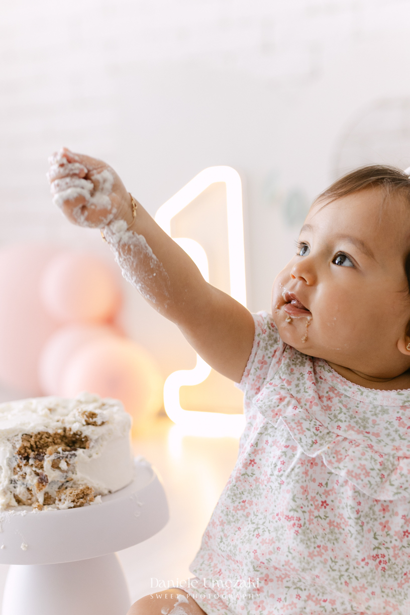 Smash the Cake da Luiza realizado em estúdio em Mogi das Cruzes, com bolo da Ume Doces. Ensaio fotográfico infantil registrando os primeiros momentos do aniversário de 1 ano com leveza, diversão e afeto.