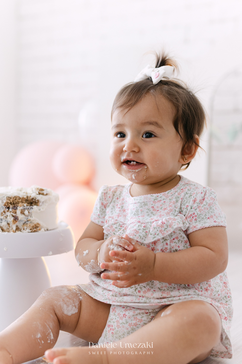 Smash the Cake da Luiza realizado em estúdio em Mogi das Cruzes, com bolo da Ume Doces. Ensaio fotográfico infantil registrando os primeiros momentos do aniversário de 1 ano com leveza, diversão e afeto.