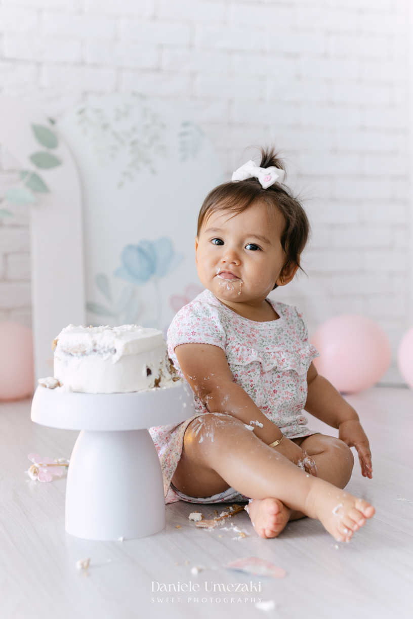 Smash the Cake da Luiza realizado em estúdio em Mogi das Cruzes, com bolo da Ume Doces. Ensaio fotográfico infantil registrando os primeiros momentos do aniversário de 1 ano com leveza, diversão e afeto.