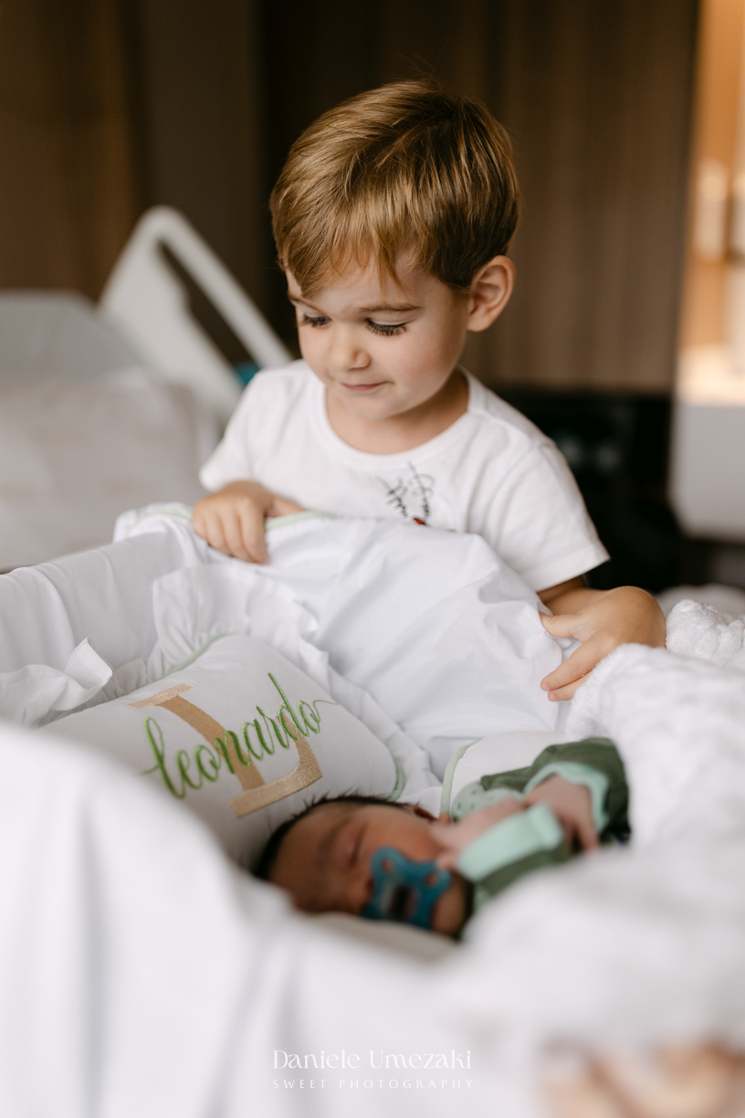 Encontro de irmãos na Maternidade São Luiz Star em São Paulo, registrando o momento em que Bernardo conhece o pequeno Leonardo pela primeira vez, fotografado por Dani Umezaki