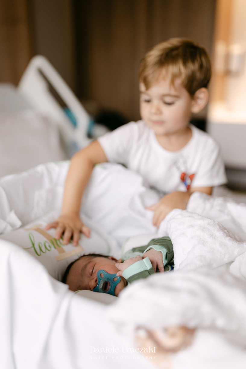 Encontro de irmãos na Maternidade São Luiz Star em São Paulo, registrando o momento em que Bernardo conhece o pequeno Leonardo pela primeira vez, fotografado por Dani Umezaki