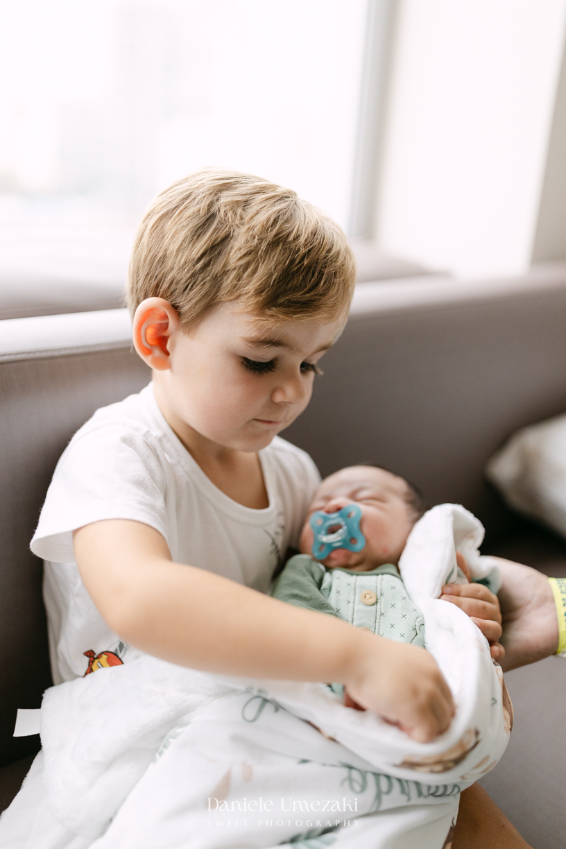 Encontro de irmãos na Maternidade São Luiz Star em São Paulo, registrando o momento em que Bernardo conhece o pequeno Leonardo pela primeira vez, fotografado por Dani Umezaki