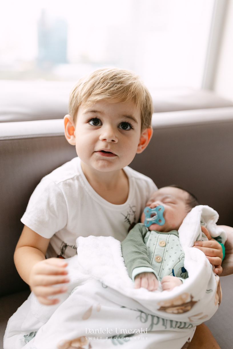 Encontro de irmãos na Maternidade São Luiz Star em São Paulo, registrando o momento em que Bernardo conhece o pequeno Leonardo pela primeira vez, fotografado por Dani Umezaki