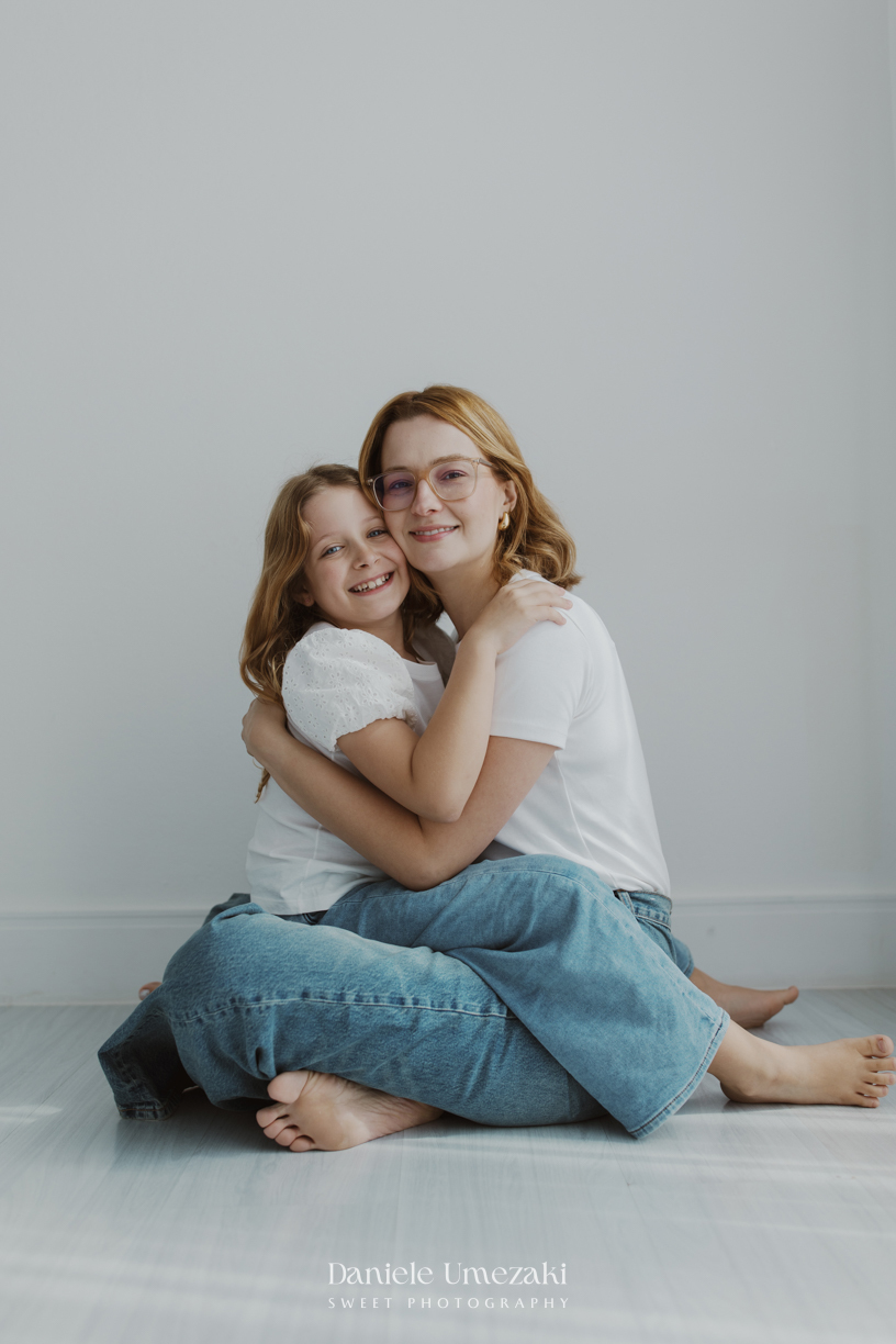 Ensaio de família em estúdio em Mogi das Cruzes com Kamilla e suas duas filhas, registrando a conexão, os abraços e a beleza da infância de forma leve, natural e atemporal por Dani Umezaki.