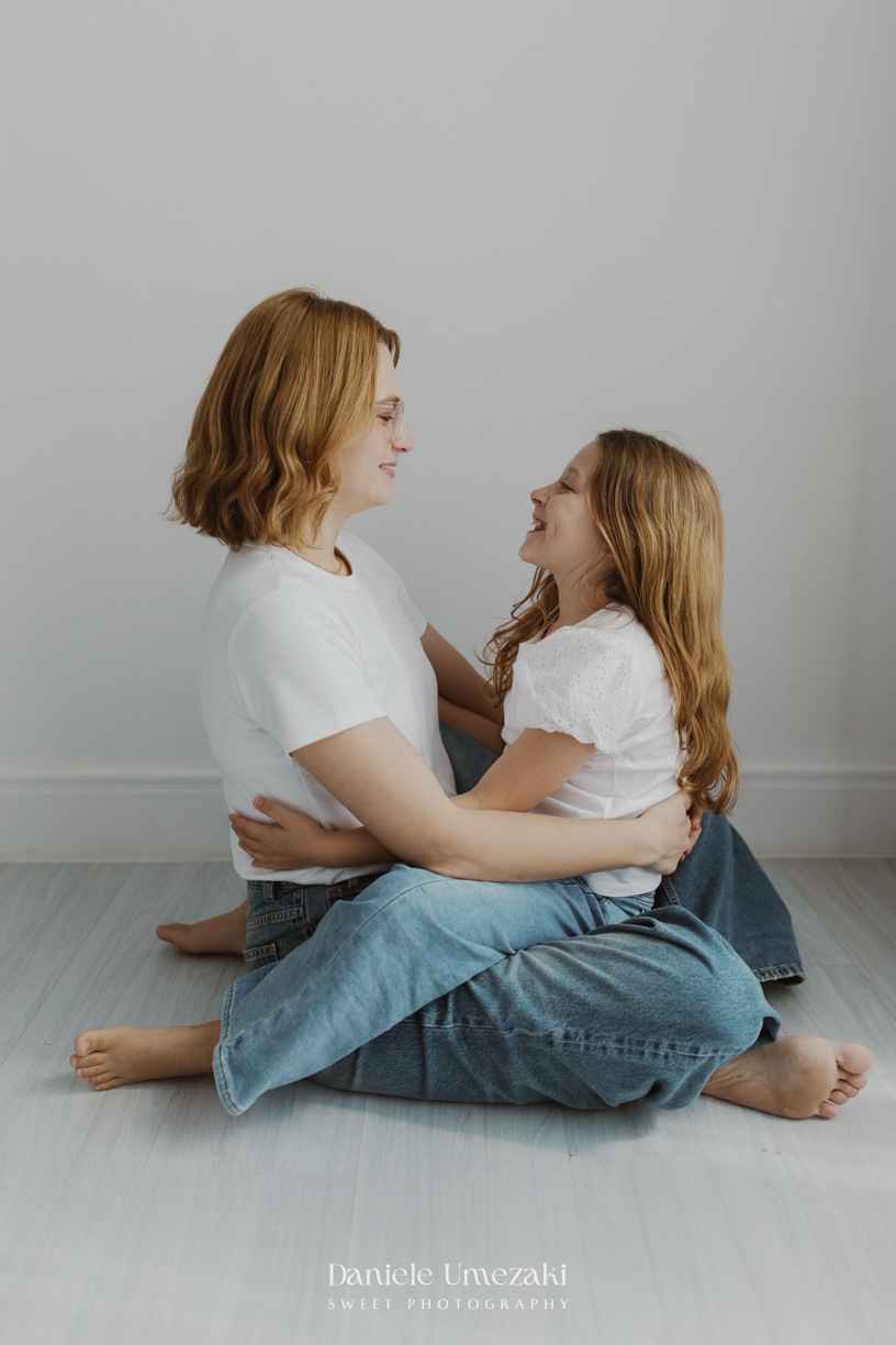 Ensaio de família em estúdio em Mogi das Cruzes com Kamilla e suas duas filhas, registrando a conexão, os abraços e a beleza da infância de forma leve, natural e atemporal por Dani Umezaki.