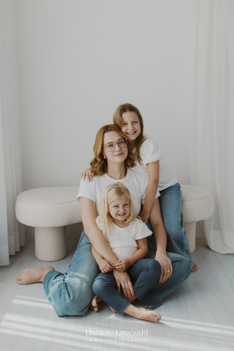Ensaio de família em estúdio em Mogi das Cruzes com Kamilla e suas duas filhas, registrando a conexão, os abraços e a beleza da infância de forma leve, natural e atemporal por Dani Umezaki.
