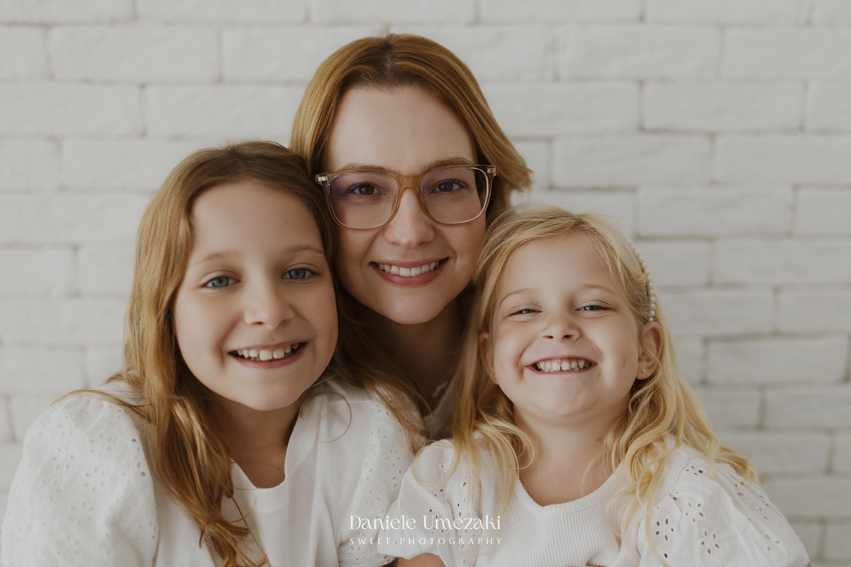 Ensaio de família em estúdio em Mogi das Cruzes com Kamilla e suas duas filhas, registrando a conexão, os abraços e a beleza da infância de forma leve, natural e atemporal por Dani Umezaki.