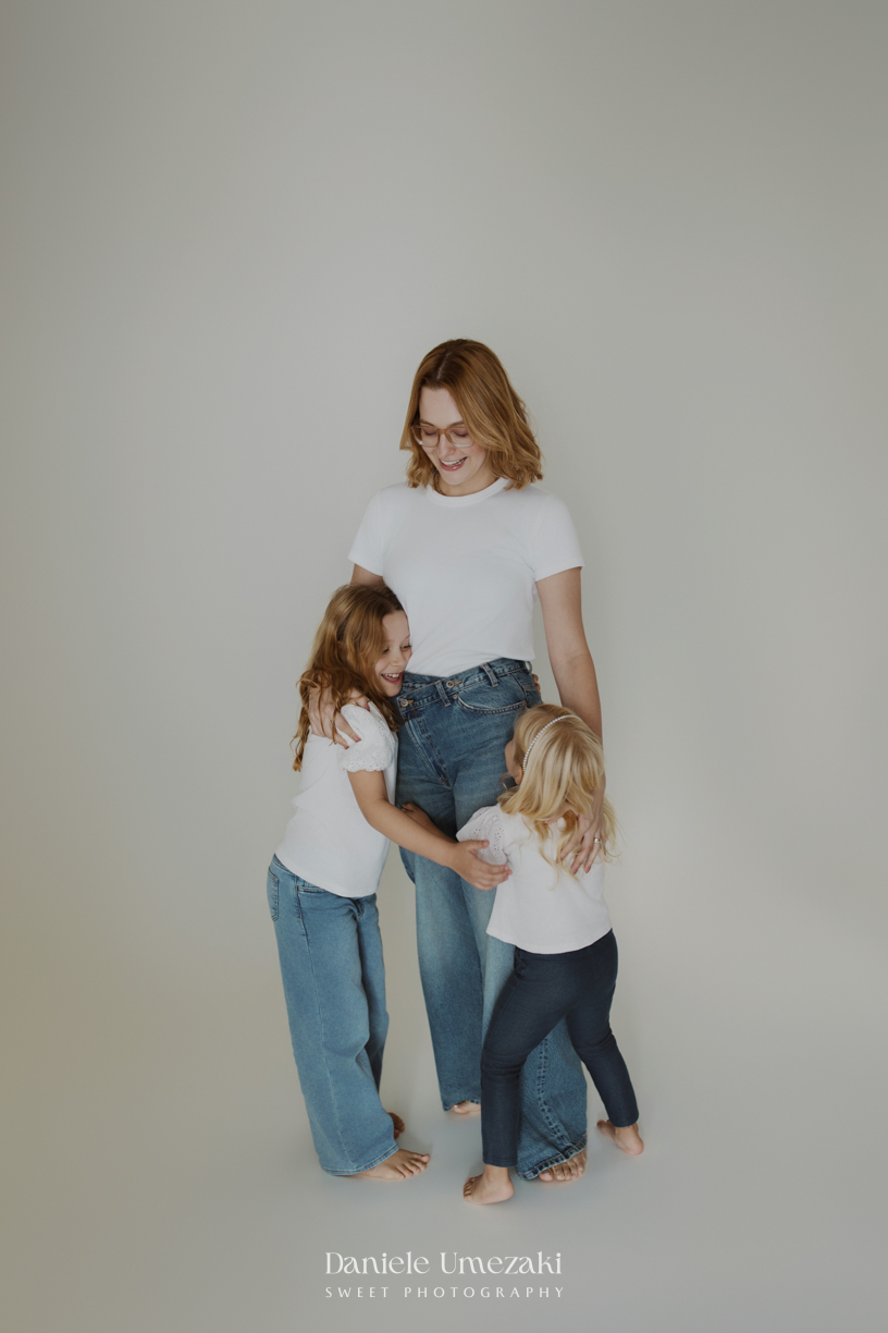 Ensaio de família em estúdio em Mogi das Cruzes com Kamilla e suas duas filhas, registrando a conexão, os abraços e a beleza da infância de forma leve, natural e atemporal por Dani Umezaki.
