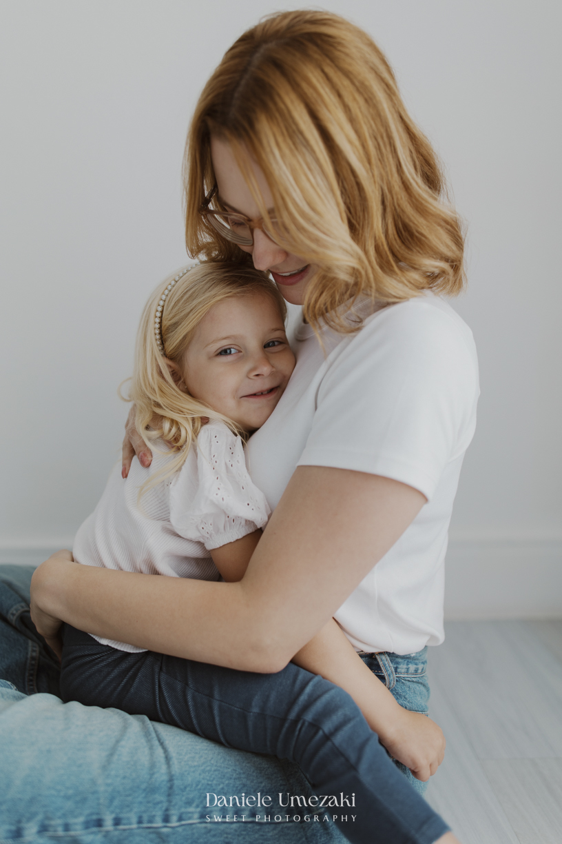 Ensaio de família em estúdio em Mogi das Cruzes com Kamilla e suas duas filhas, registrando a conexão, os abraços e a beleza da infância de forma leve, natural e atemporal por Dani Umezaki.