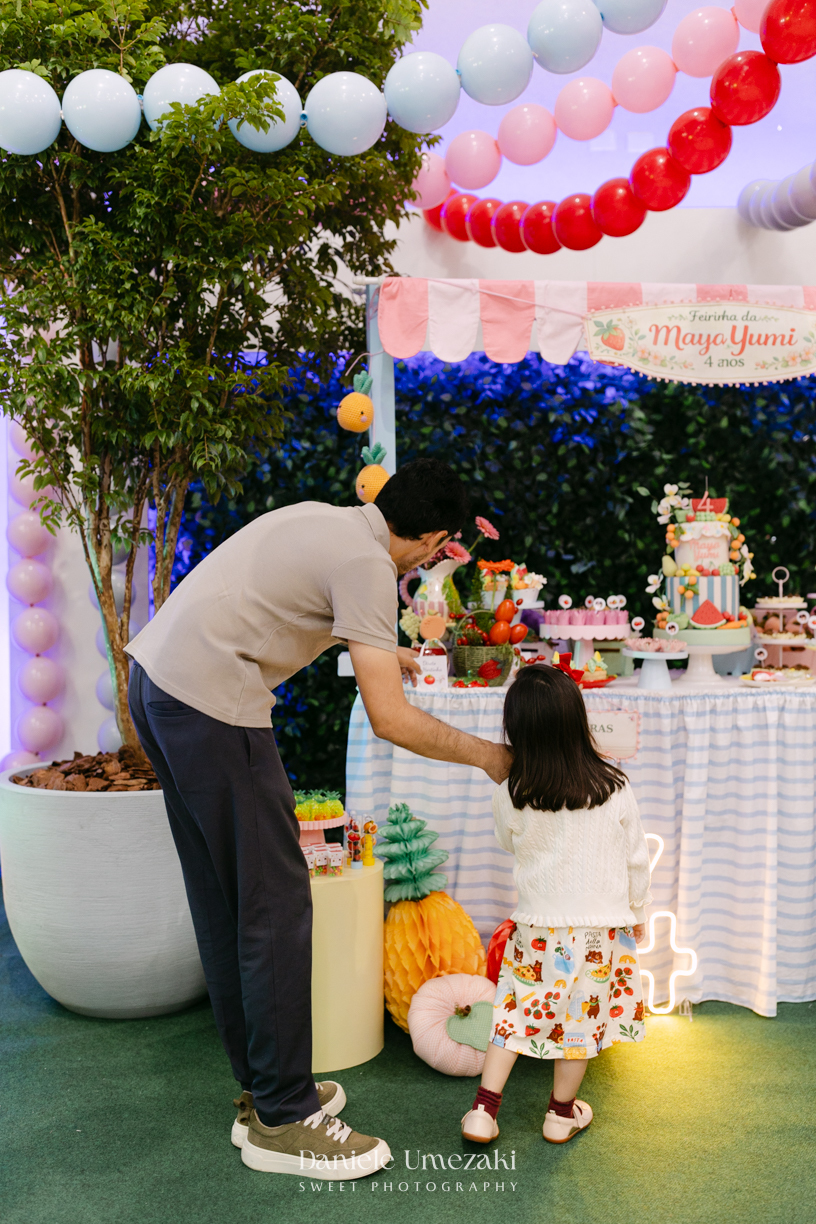 Maya sorrindo em frente à decoração de feira criada pela Panda Pink durante seu aniversário de 4 anos no Buffet Santa Arruaça, em Arujá.