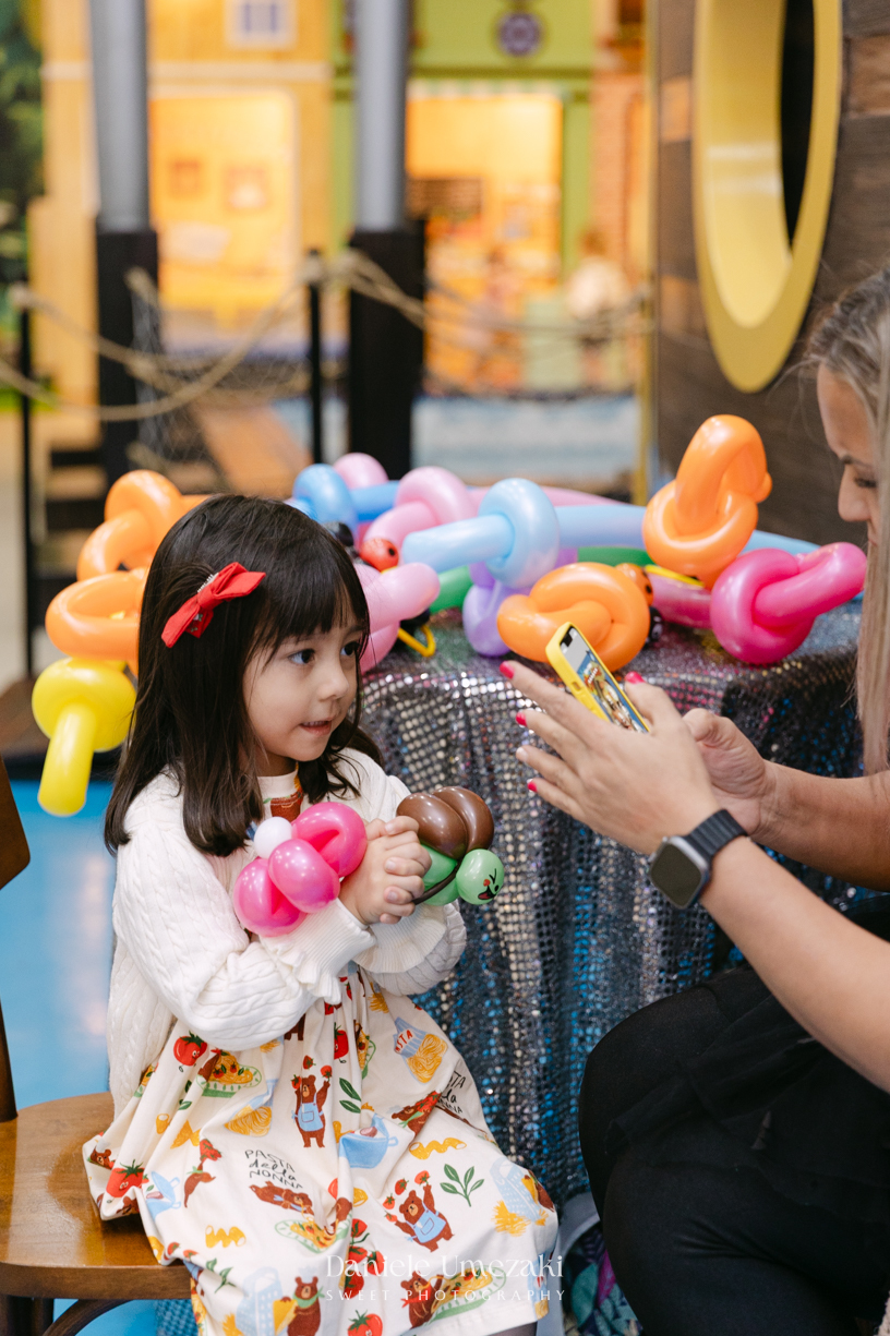 Maya sorrindo em frente à decoração de feira criada pela Panda Pink durante seu aniversário de 4 anos no Buffet Santa Arruaça, em Arujá.