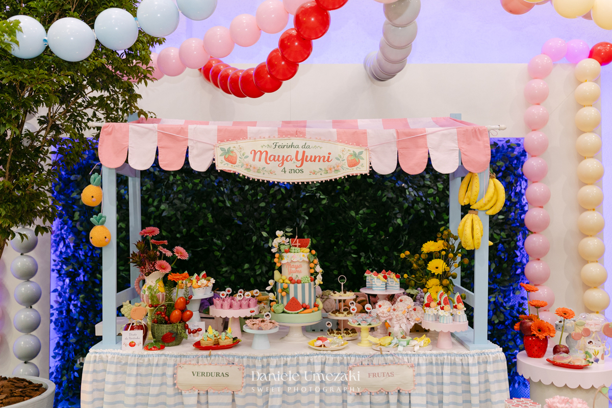 Maya sorrindo em frente à decoração de feira criada pela Panda Pink durante seu aniversário de 4 anos no Buffet Santa Arruaça, em Arujá.