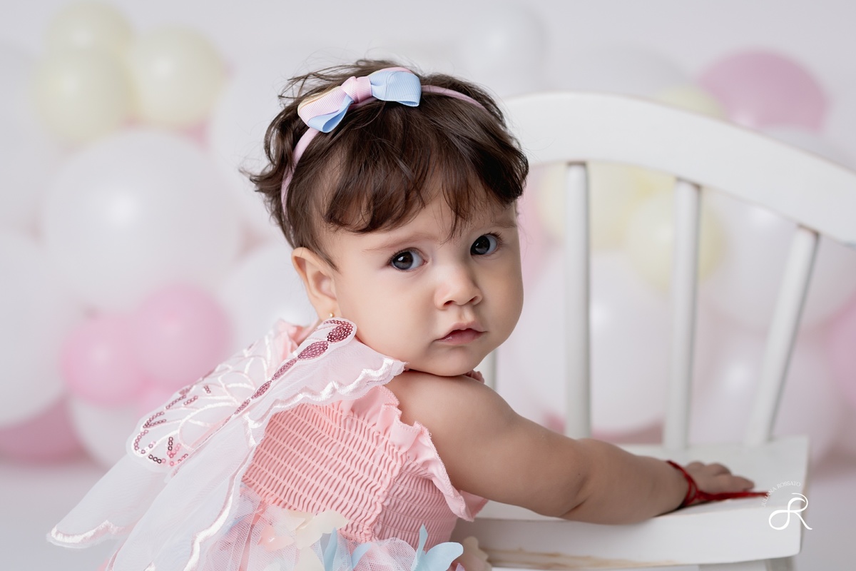 Ensaio smash de 1 ano com bexigas coloridas entre branco, rosa e amarelo e tema clean para comemorar seu primeiro aniversário de forma atemporal.