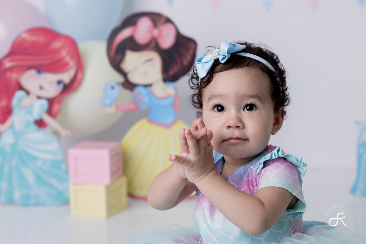 Ensaio smash de 1 ano com bexigas coloridas rosa, amarelo e azul, tema princesas para comemorar seu primeiro aniversário, ariel, branca de neve, cinderela, bela, pequena sereia, ensaio com bolo, ensaio com fruta