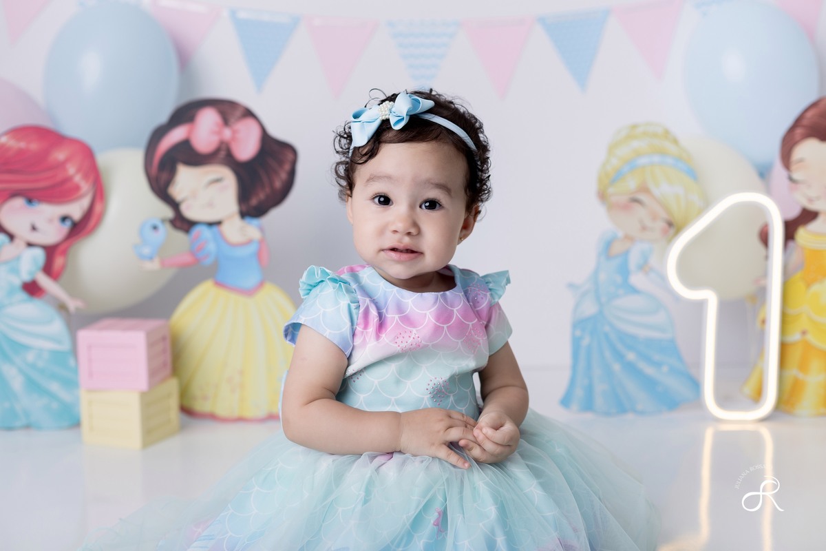 Ensaio smash de 1 ano com bexigas coloridas rosa, amarelo e azul, tema princesas para comemorar seu primeiro aniversário, ariel, branca de neve, cinderela, bela, pequena sereia, ensaio com bolo, ensaio com fruta