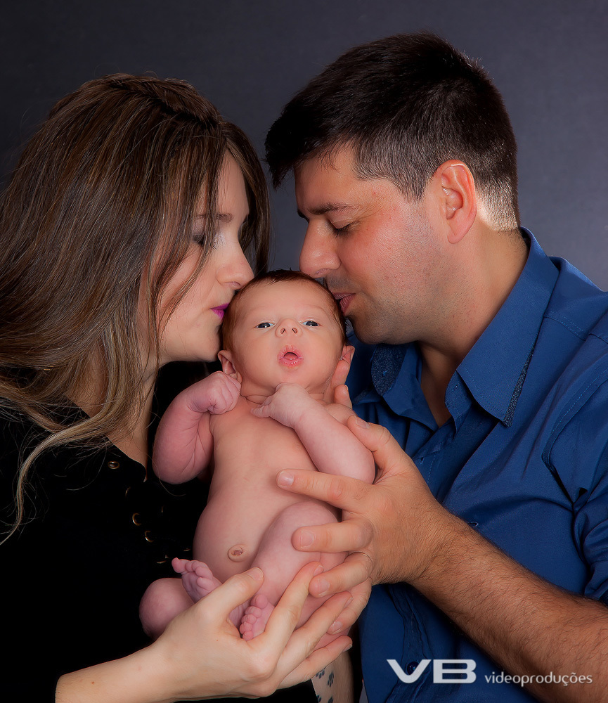Bebê peladinho com os pais beijando o rosto