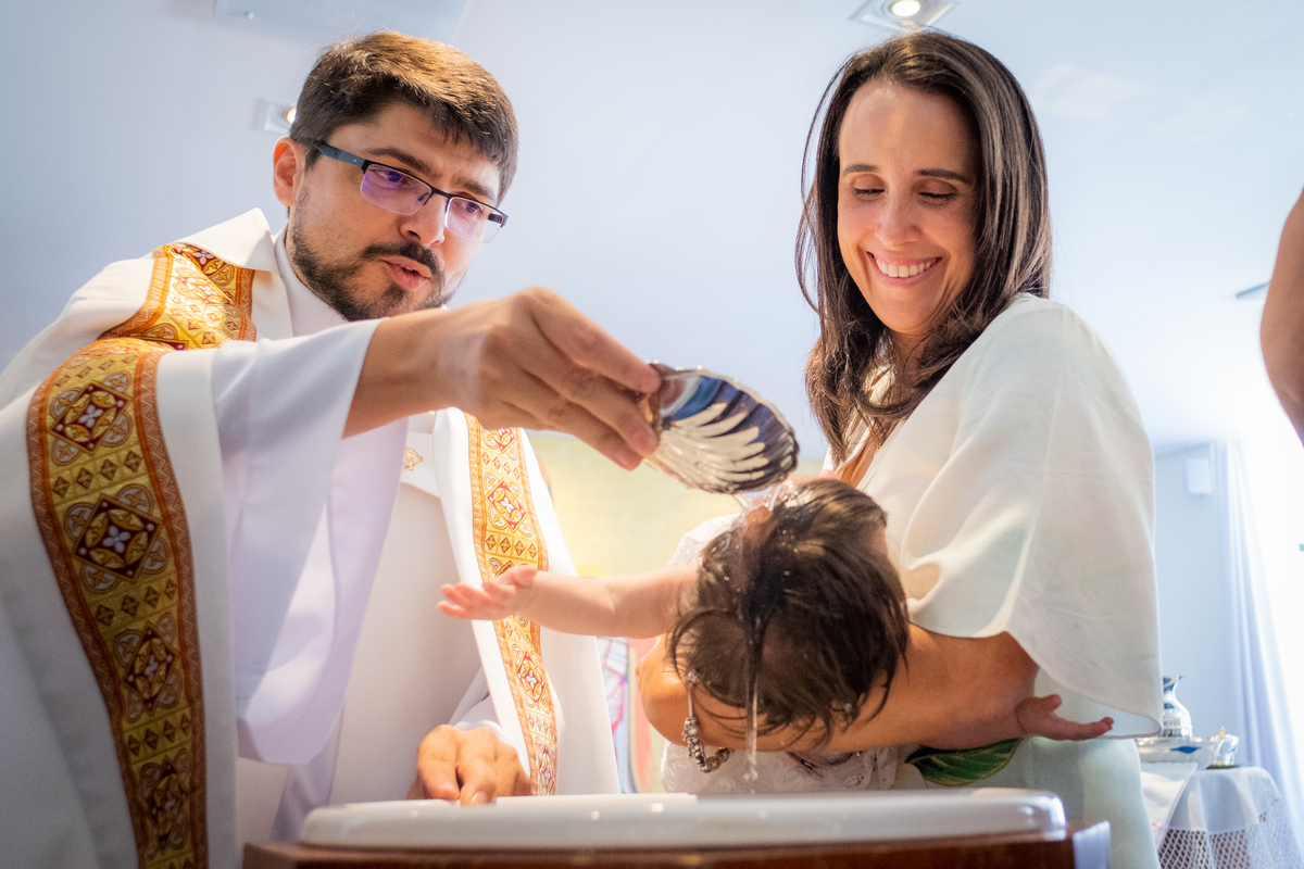 Padre batizando e mãe sorrindo e olhando para o bebê