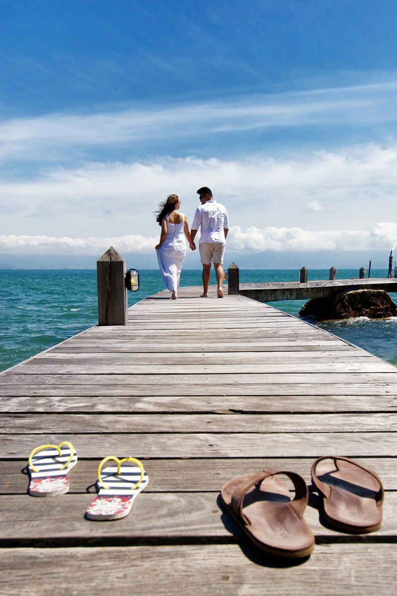 noivos caminham sobre o pier e deixam os chinelos