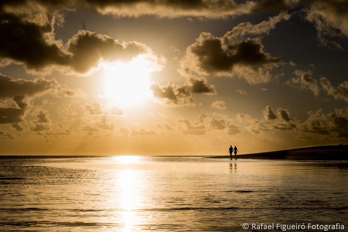 casal distante caminhando pontal maria farinha sol reflexo na agua ceu amarelado com nuvens paisagem linda