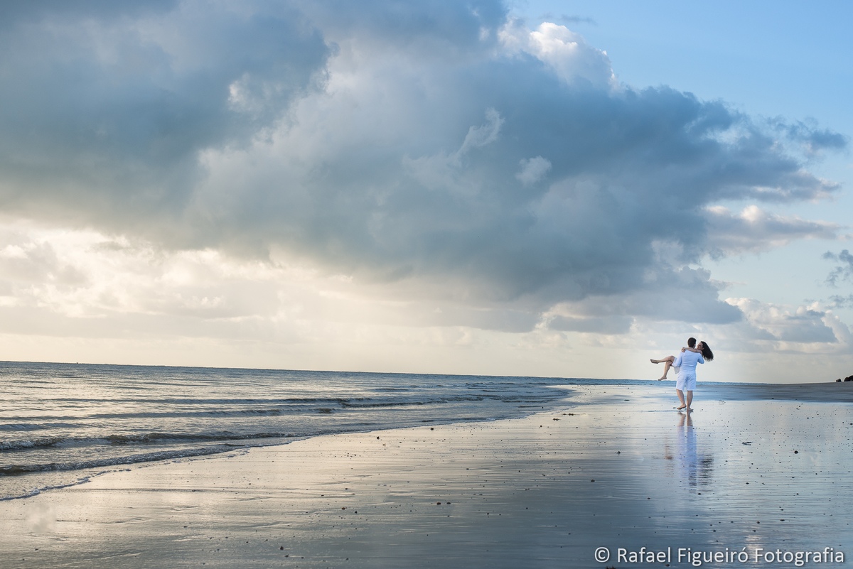 noivo segurando noiva no colo praia ceu mar nuvens distante