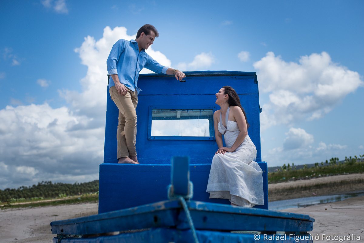 casal sentado sobre barco azul encalhado areia maria farinha