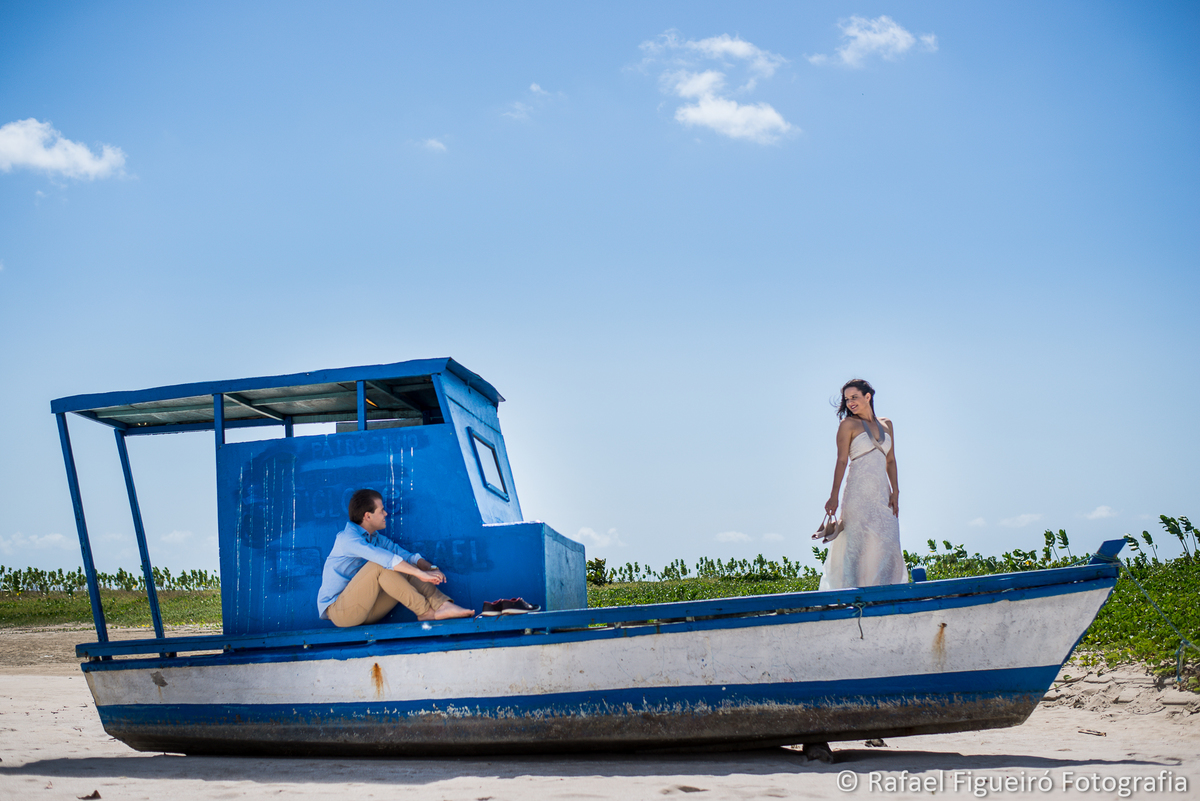 casal sobre barco azul encalhado areia noivo sentado noiva em pe