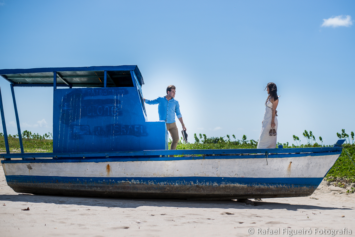 casal sobre barco azul encalhado areia noivo em direçao da noiva em pe