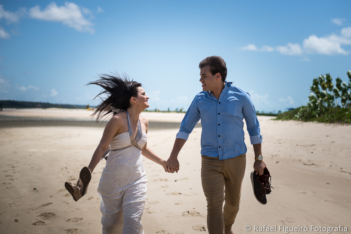 casal correndo se olhando sorrindo areia praia rio mangue sapatos nas mãos
